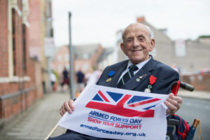 Veterans holding the Armed Forces Day flag smiling at the camera. 