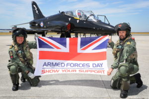 RAF personnel in front of their aircraft holding an Armed Forces Day flag.