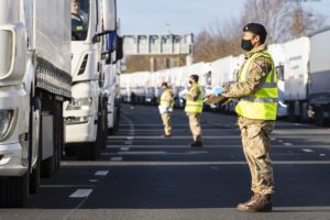 Soldier in high visibility jacked looks up to the cab of a lorry.