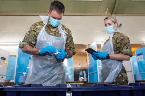 Two personnel wearing PPE over their uniforms prepare testing equipment.