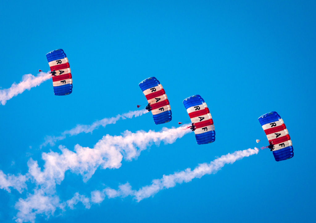 RAF parachutists are photographed from below against a blue sky
